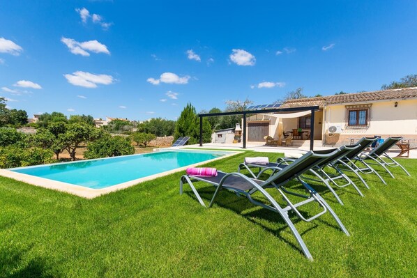 A swimming pool with lounge chairs, a covered patio, and a house with a tiled roof. - Country House 'Calderitx' with Private Pool, Wi-Fi and Air Conditioning (Ariany)