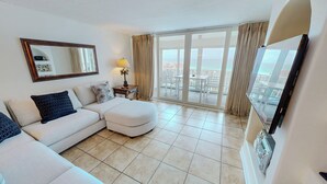 Una sala de estar moderna con sofá, reposapiés, lámpara, televisor y balcón con vistas.