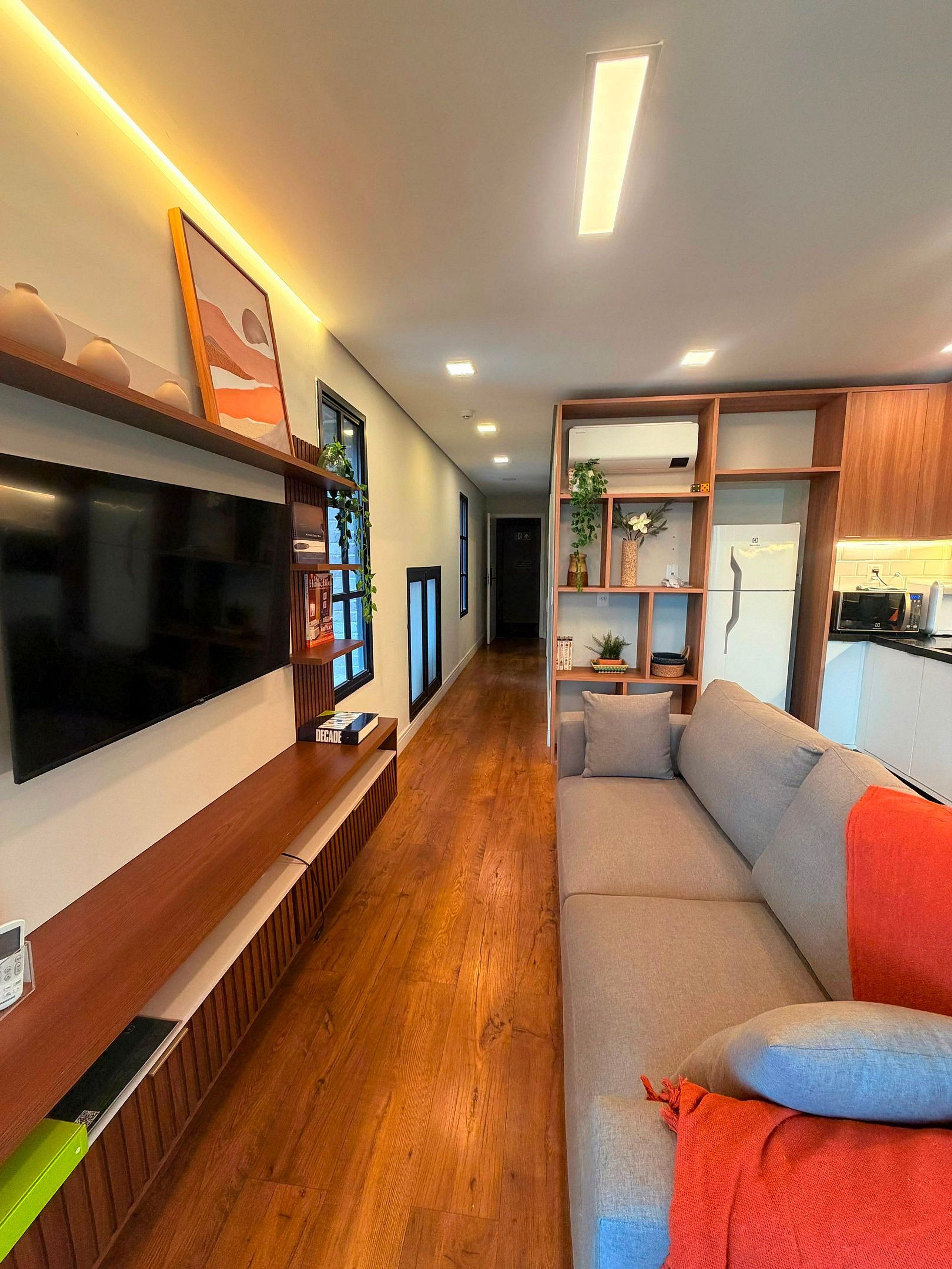 Una sala de estar moderna con un televisor de pantalla plana, mueble de entretenimiento de madera y un sofá con cojines.
