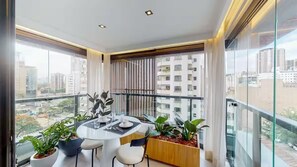 A modern balcony with a dining table, chairs, potted plants, and a city view. - Arte Itaim (São Paulo)