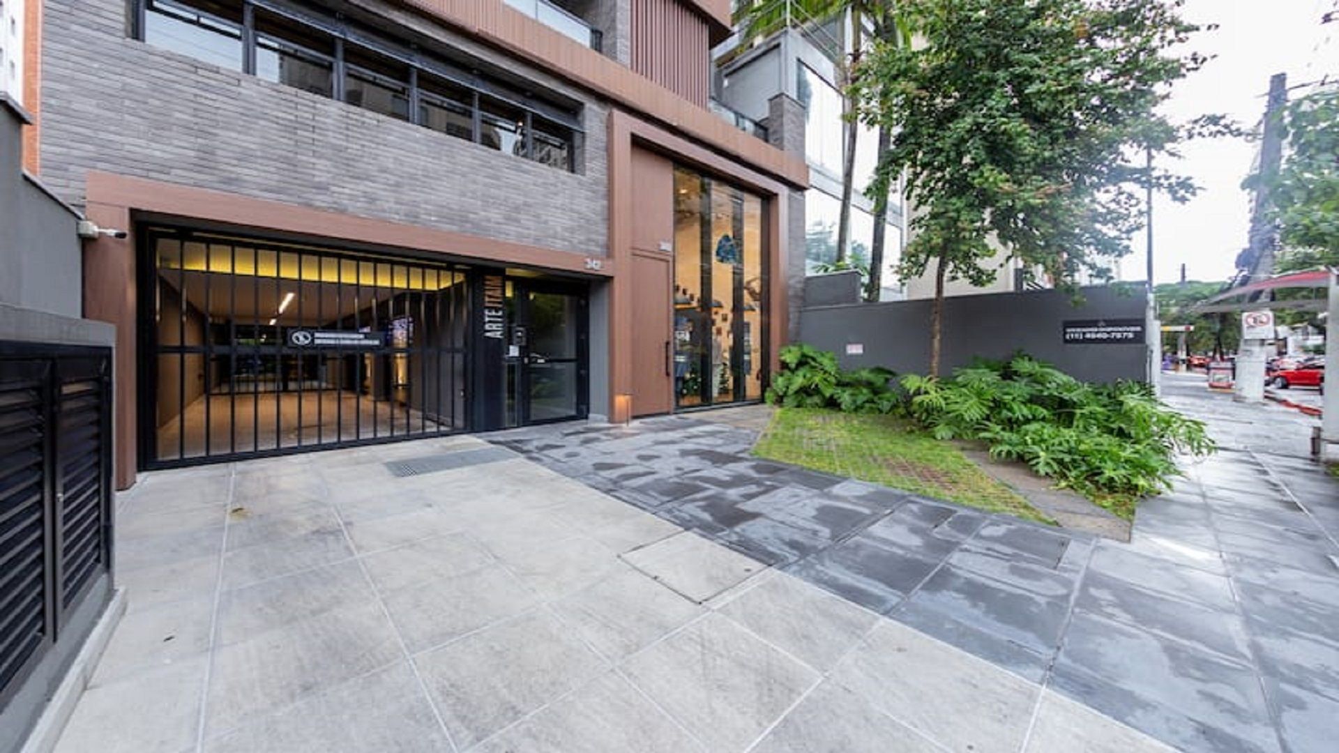 A modern building with a gated entrance, a paved walkway, and a small landscaped area with plants.