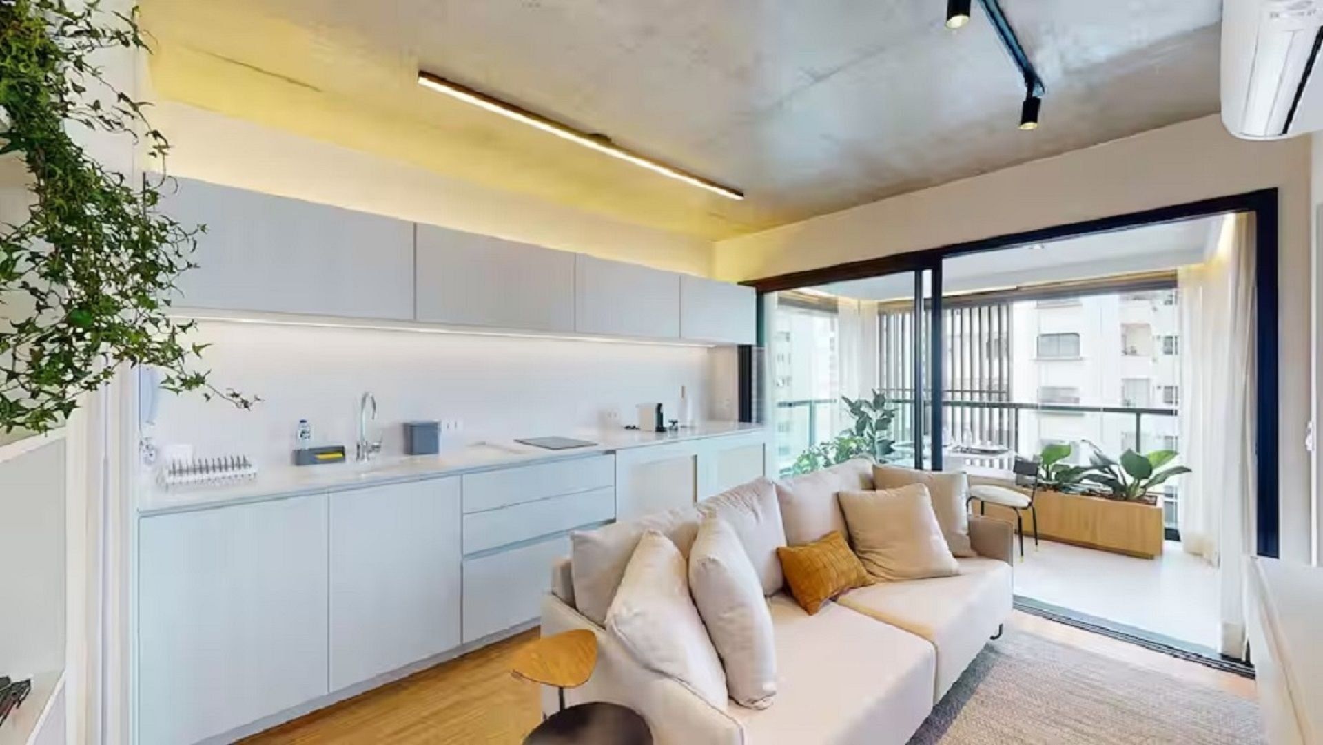 Ein moderner Wohnraum mit Küche, einer Couch und einem Balkon mit Pflanzen.