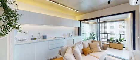 A modern living space with a kitchen, a sofa, and a balcony with plants.