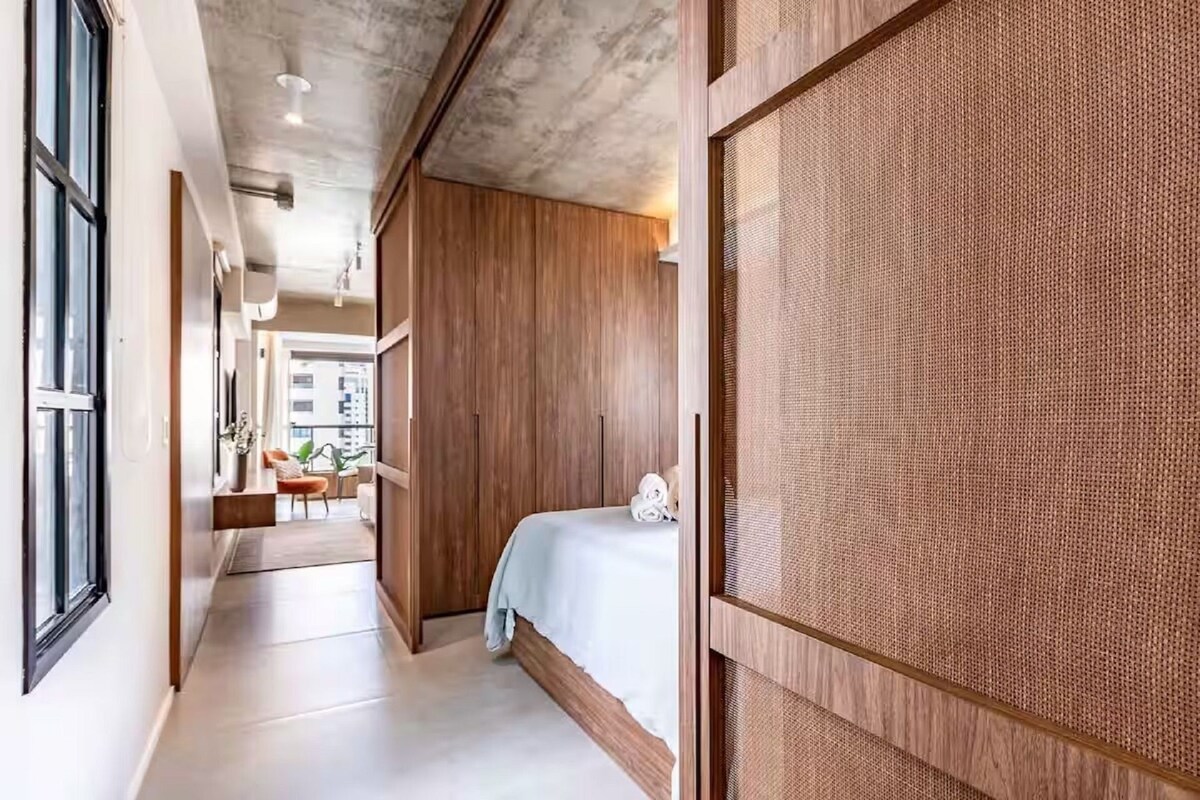 A hotel room with a bed, a wooden wardrobe, a window, and a view of the outside.