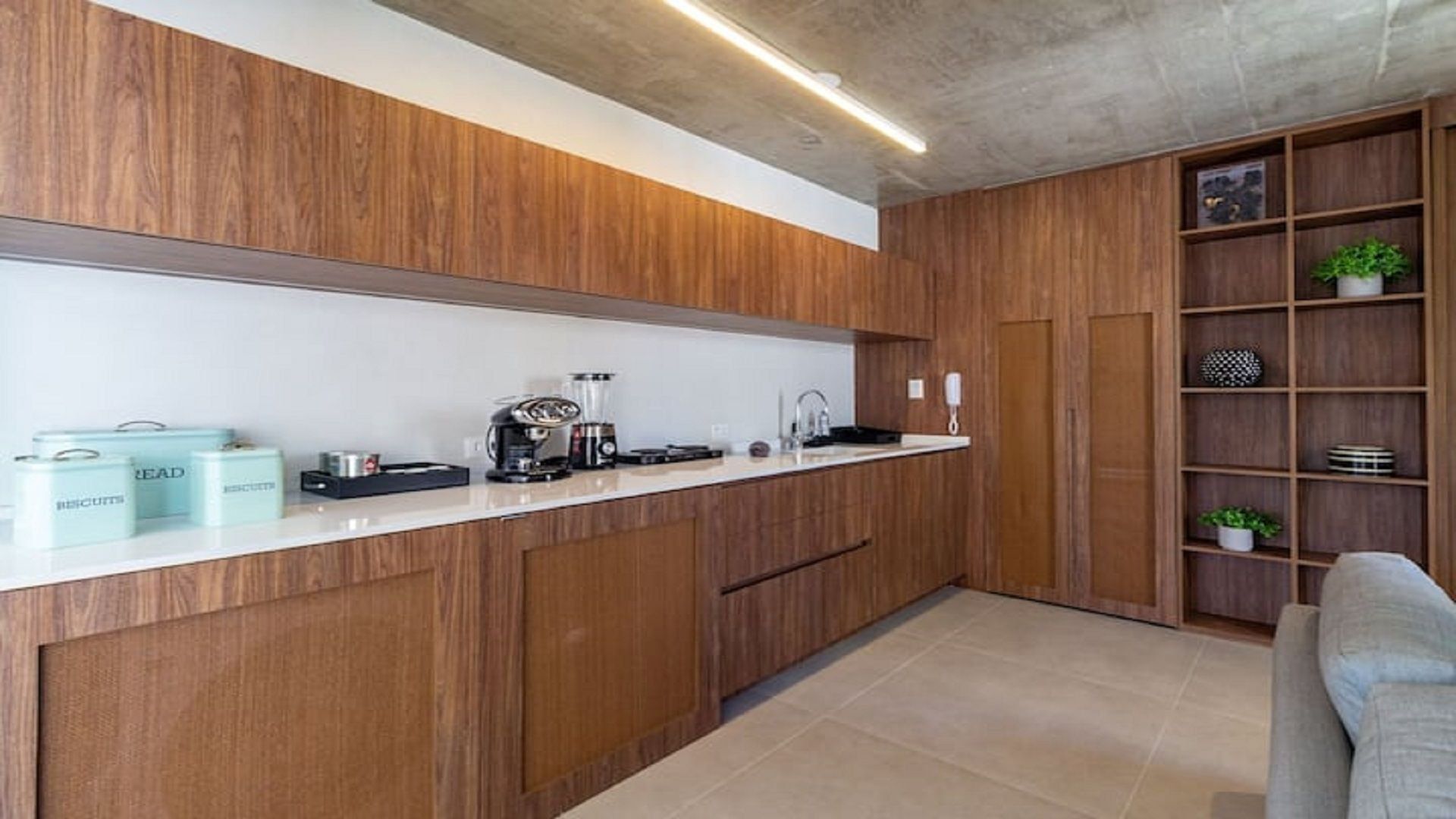 A modern kitchen with wooden cabinets, a white countertop, and a built-in shelving unit with decorative items.
