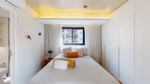 Ein modernes Hotelzimmer mit einem großen Bett, einem Fenster mit Vorhängen, einem Nachttisch und einem Kleiderschrank.