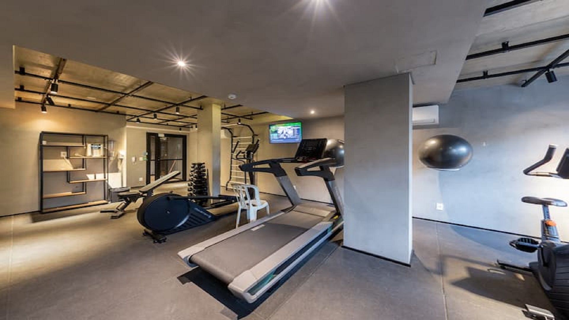 A modern gym with treadmills, weight machines, and a television screen.