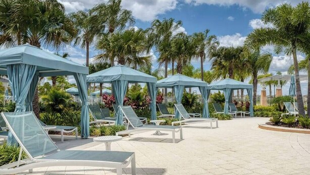 Un área de piscina en un resort con tumbonas, toldos azules y palmeras.