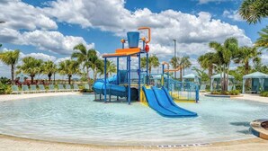 Un parque acuático con un tobogán azul, una zona de juegos de agua y sillas de descanso alrededor de una piscina.