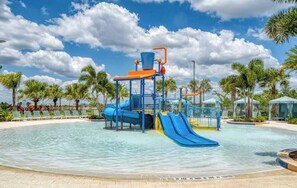 Ein Wasserpark mit einer blauen Rutsche, einem Wasserspielbereich und Liegestühlen rund um einen Pool.