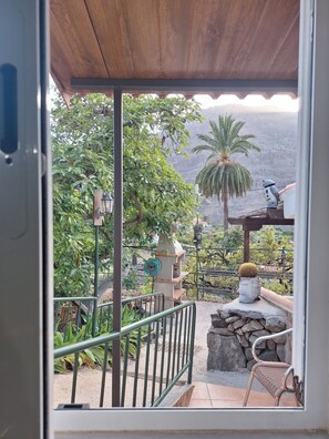 Une vue depuis un balcon, avec un plafond en bois, un mur en pierre, un palmier et une chaise.