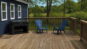 Une terrasse avec un barbecue, deux fauteuils Adirondack et une maison aux murs bleus et aux fenêtres blanches.