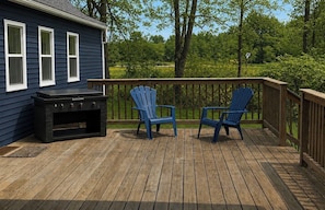 A deck with a grill, two Adirondack chairs, and a house with blue siding and white windows.
