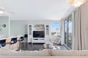 Ein modernes Wohnzimmer mit Flachbildfernseher, einer Essecke mit Barhocker, einer Couch und einem großen Fenster mit Blick auf die Stadt.