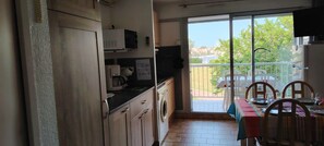 A kitchen with a washing machine, a microwave, and a dining area with chairs and a table. - STUDIO CABIN 4 PERSONS (Agde)