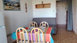 Ein Essbereich mit einem Tisch für vier Personen, einem grauen Sofa, einem Kühlschrank und einer Tür zu einem anderen Raum.
