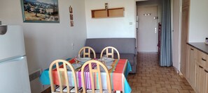 A dining area with a table set for four, a gray sofa, a refrigerator, and a door leading to another room. - STUDIO CABIN 4 PERSONS (Agde)