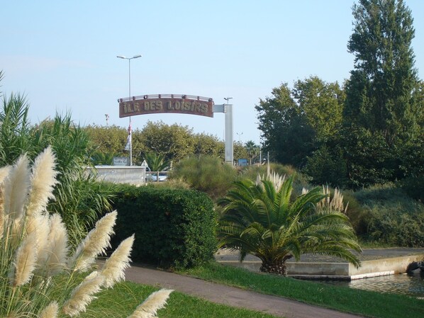 A sign reading 'ÎLE DES LOISIRS' with a pathway and greenery in the foreground. - STUDIO CABIN 4 PERSONS (Agde)