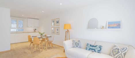 A modern living room with a sofa, a coffee table, and a dining area with chairs and a table.