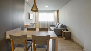 En moderne stue med spiseområde, sofa, tv og en pendel.
