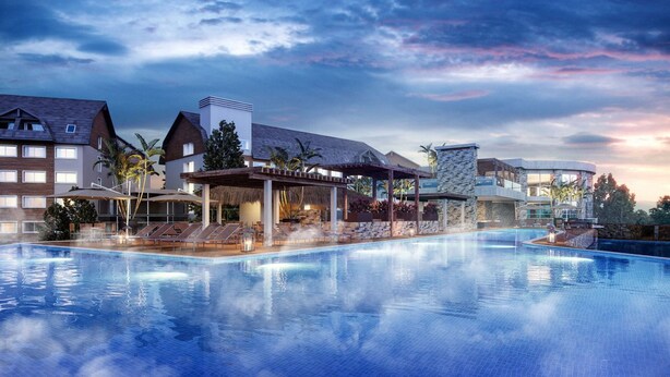 En swimmingpool med liggestole og et overdækket område, omgivet af bygninger med moderne arkitektur og en solnedgangshimmel.