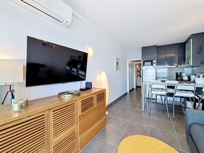 Ein modernes Wohnzimmer mit Flachbildfernseher, einer Holz-Unterhaltungseinheit und einem Essbereich, mit einer Küche im Hintergrund.