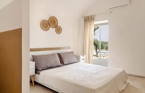 Ein Schlafzimmer mit Bett, Nachttisch, einer Wanddekoration und Blick ins Freie.