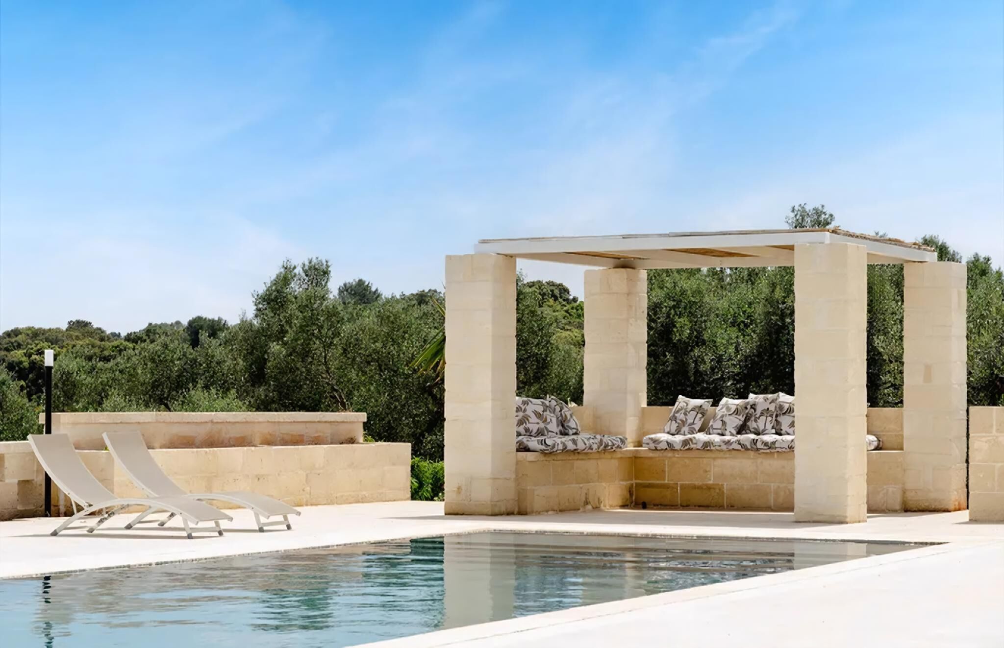 Ein Poolbereich mit Liegestühlen, einer Steingewölbepergola und blauem Himmel.