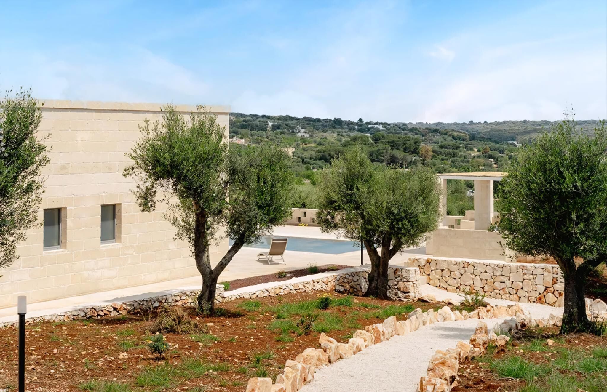 Um edifício com piscina, área de estar ao ar livre e oliveiras.