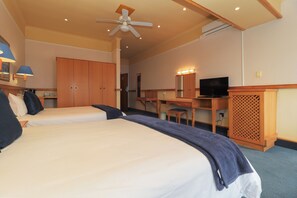 A hotel room with two beds, a desk, a television, and a ceiling fan. - The Humewood Hotel (Gqeberha)