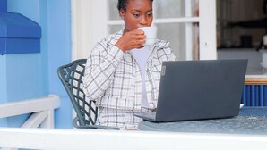 A person sitting at a table with a laptop, holding a cup.