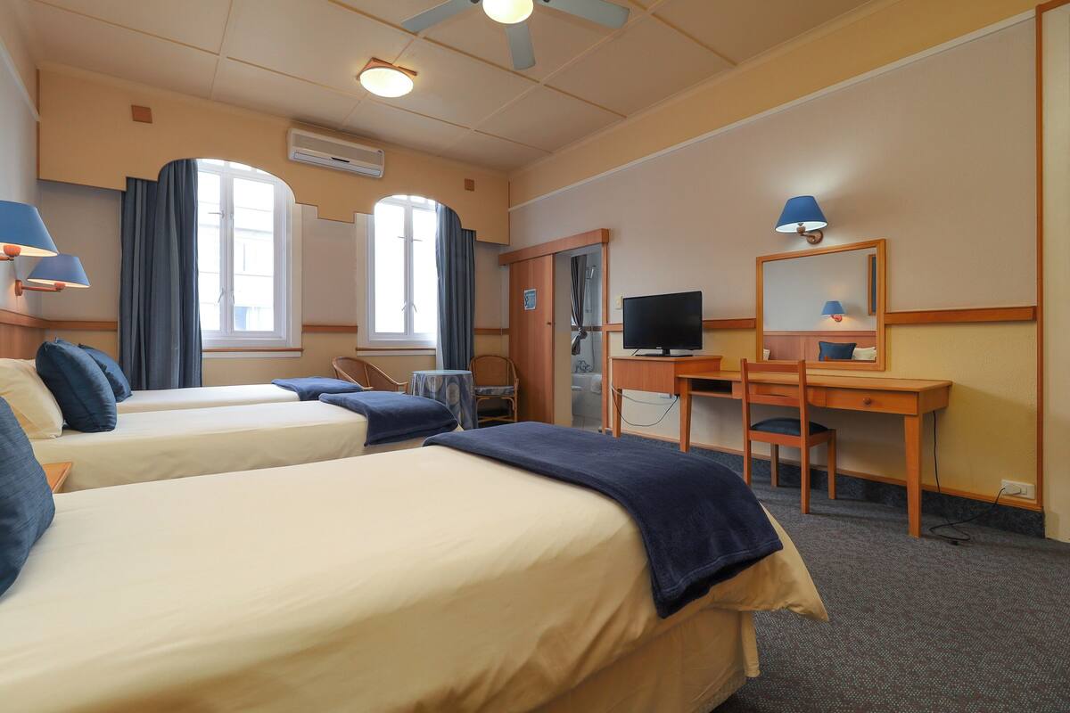 A hotel room with two beds, a desk, a television, and a mirror.