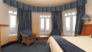 A hotel room with a bed, two chairs, a small table, and large windows with curtains.