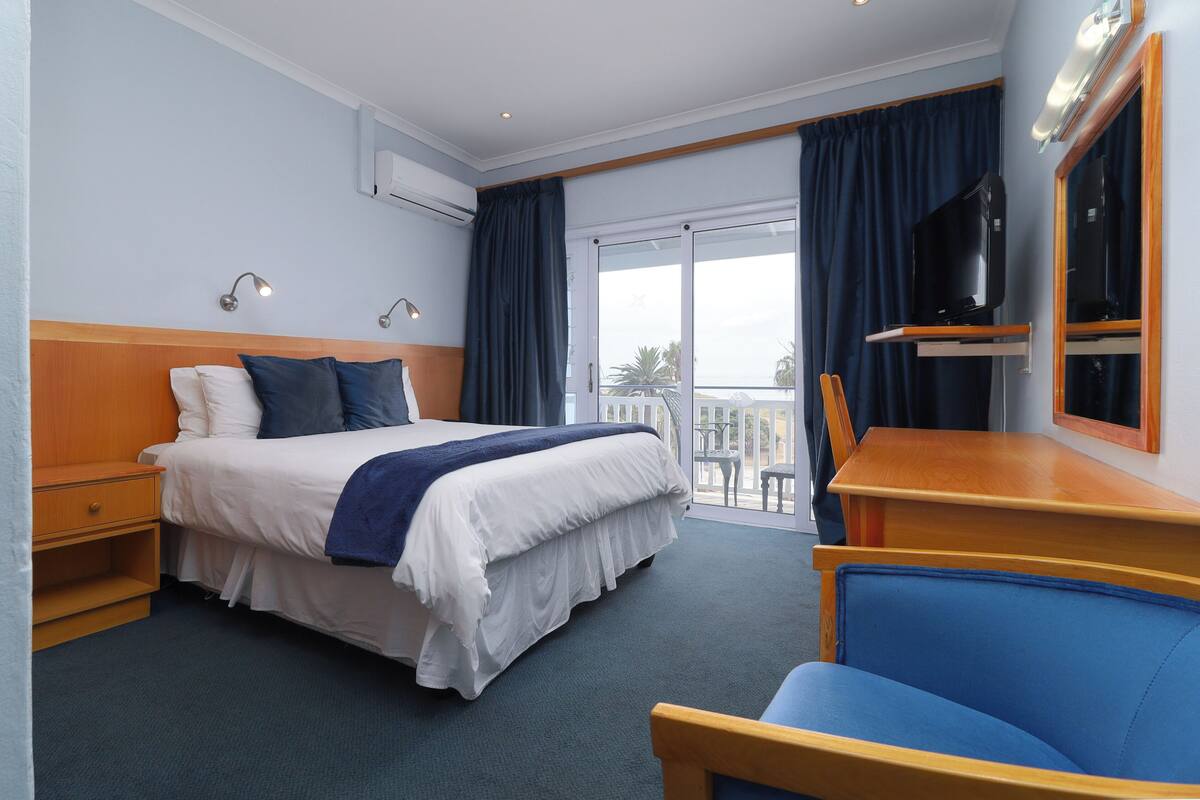 A hotel room with a bed, a desk, a chair, a TV, and a balcony with curtains.