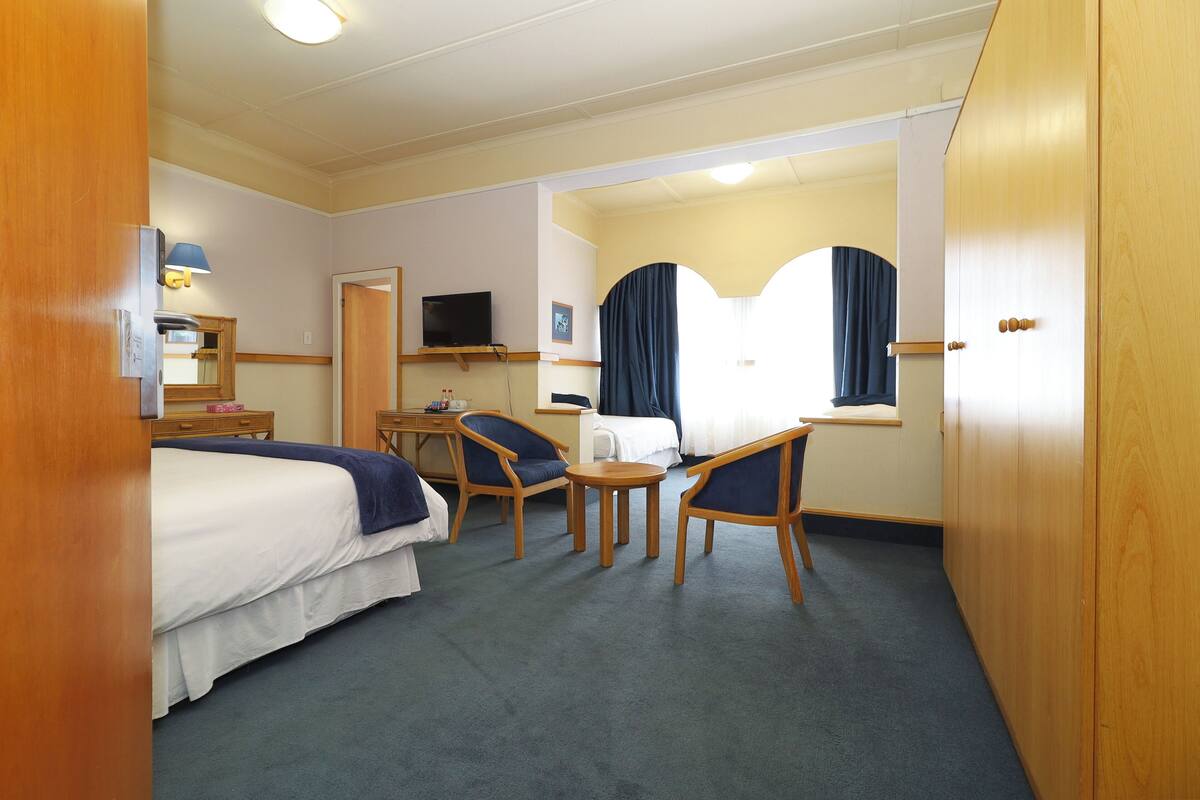 A hotel room with a bed, two chairs, a small table, a TV, and a window with curtains.
