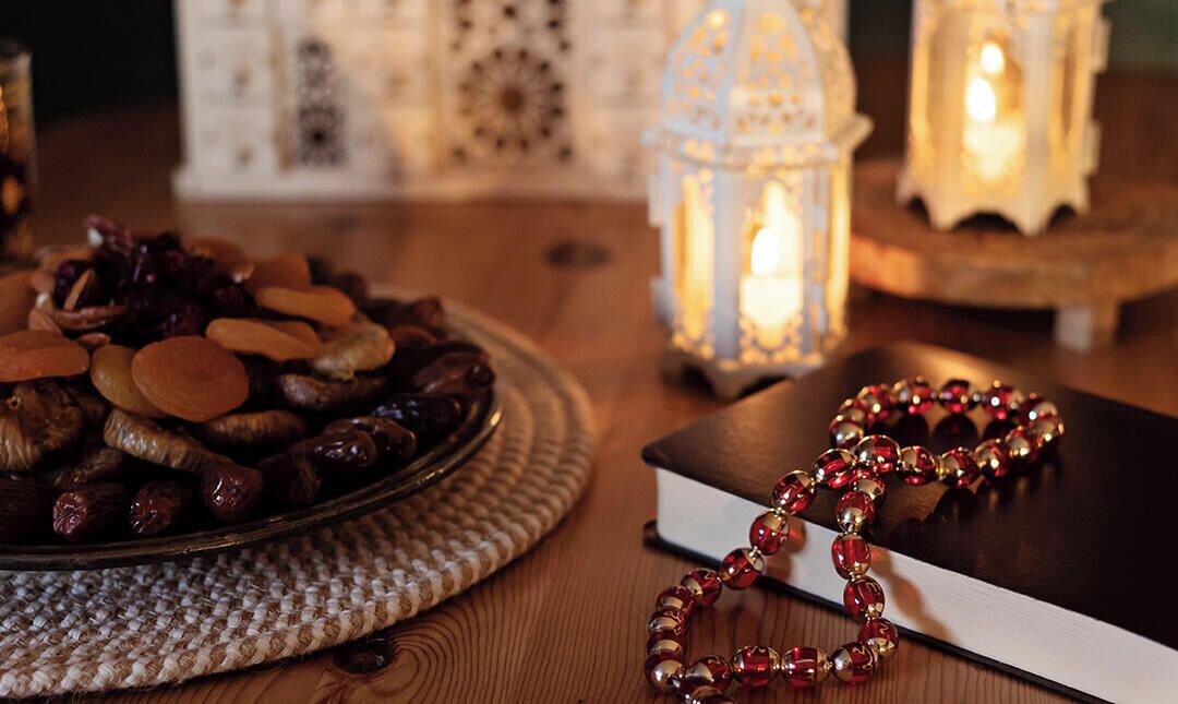 Un plato de nueces y frutas secas, un rosario y velas encendidas sobre una mesa.