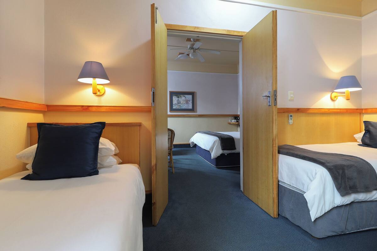 A hotel room with two beds, a chair, a ceiling fan, and two wall-mounted lamps.