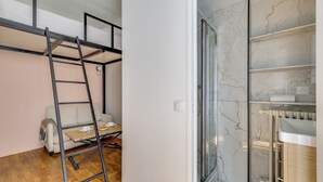 Een kamer met een houten vloer, een bank, een tafel met een schaal en een kopje, en een ladder.
