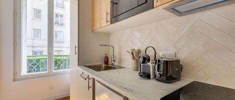 A modern kitchen with a built-in oven, a sink, and a window overlooking a residential area.