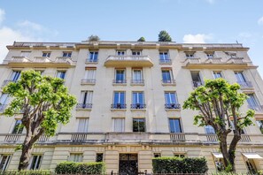 A multi-story building with balconies, a central entrance, and trees in front. - Studio 2P Near Roland Garros Stadium (Paris)