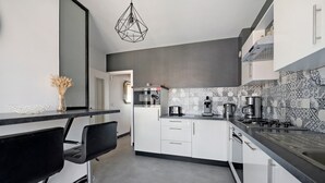 Une cuisine moderne avec des meubles blancs, un plan de travail noir et un luminaire suspendu aux motifs géométriques.