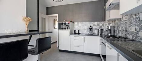 A modern kitchen with white cabinets, a black countertop, and a geometric pendant light.