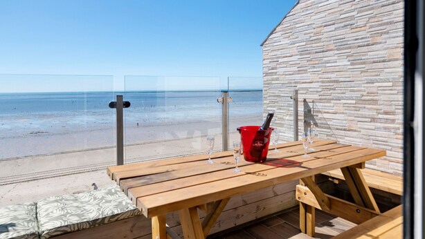 Une table en bois, avec des verres et un seau rouge, sur un balcon donnant sur une plage.