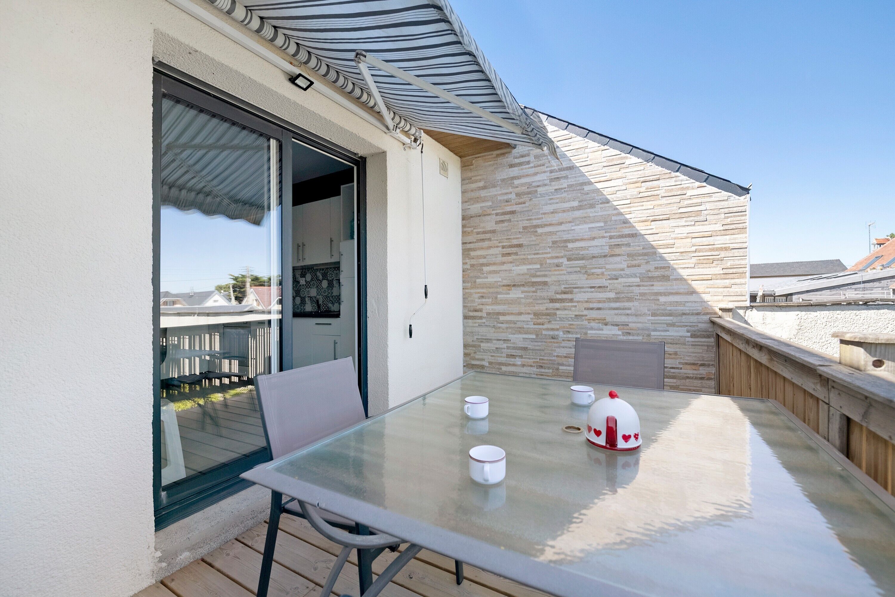 Ein Tisch mit Glasplatte, Stühle und einem weißen Sonnenschirm auf einem Balkon.