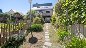 Un chemin de jardin qui mène à un bâtiment doté d’un toit en pente et de nombreuses fenêtres.