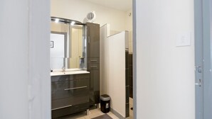 Une salle de bain moderne avec un meuble-lavabo foncé, un miroir, un sèche-cheveux et une poubelle.