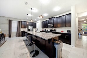 Enjoy culinary delights in this inviting kitchen, complete with rich dark cabinetry and a stunning granite island ideal for gatherings. Modern appliances and sleek bar stools make it a perfect space for cooking and entertaining. - 9BR house with private pool at Solara Resort (Kissimmee)