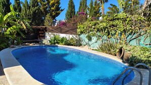 Piscina com um deck de pedra, rodeada por plantas e árvores diversas.