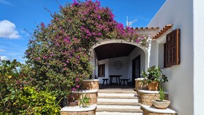 Um edifício branco com uma escadaria de pedra que leva a um arco, plantas em vasos e vista para o interior.