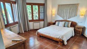 Quarto com cama de madeira, mesa de cabeceira, um radiador, janela com cortinas e luminária fixada na parede.